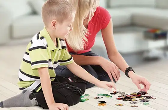 Een moeder en zoon maken samen een gepersonaliseerde puzzel; kleurrijke puzzelstukjes verspreid op de vloer.
