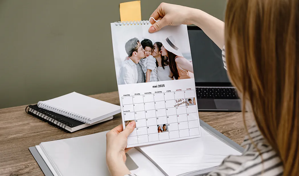 Vrouwe bekijkt gepersonaliseerde mei 2025 kalender met familiefoto's en verjaardagen.